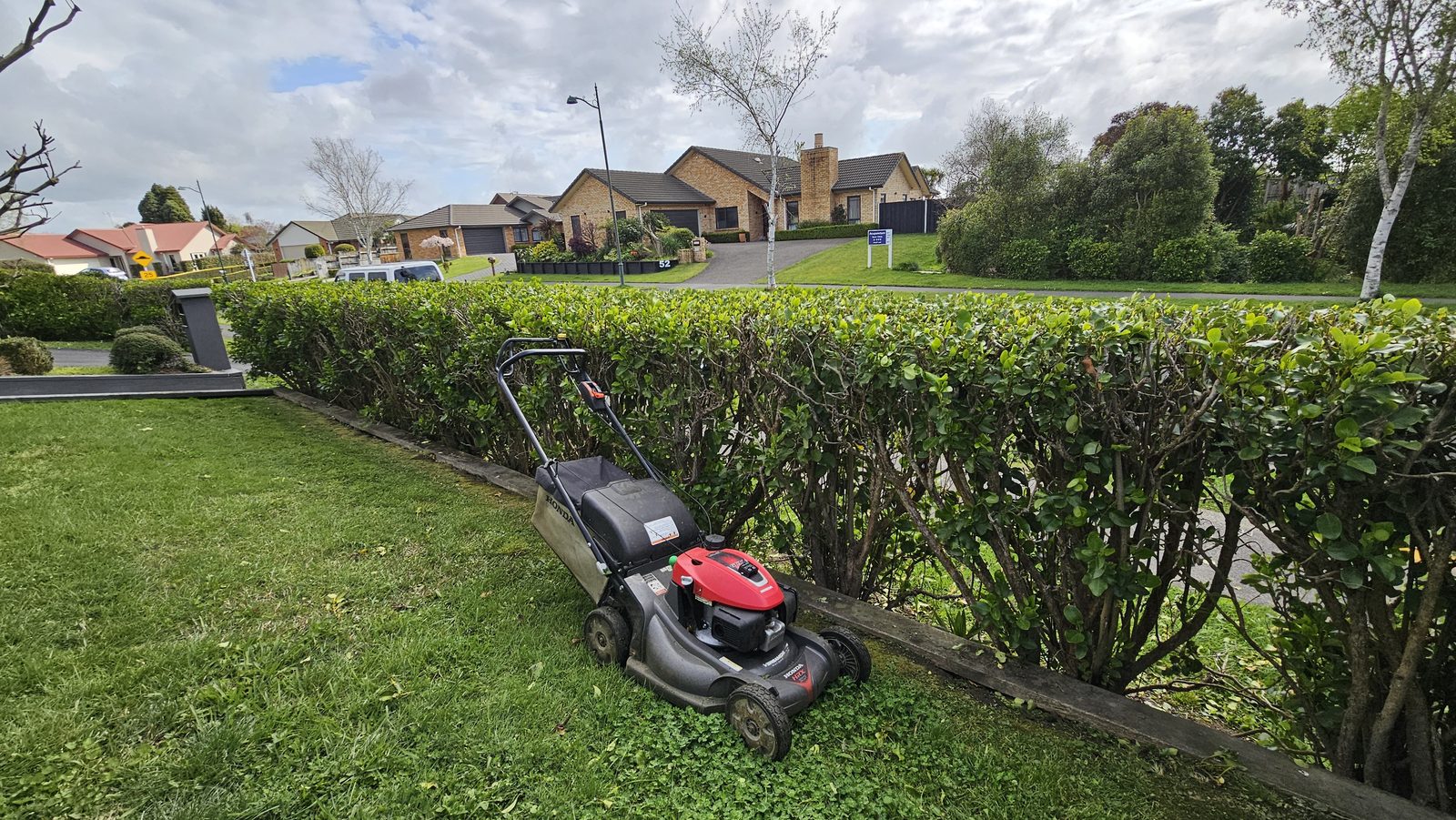 Push mower on a neatly cut lawn beside a clipped hedge